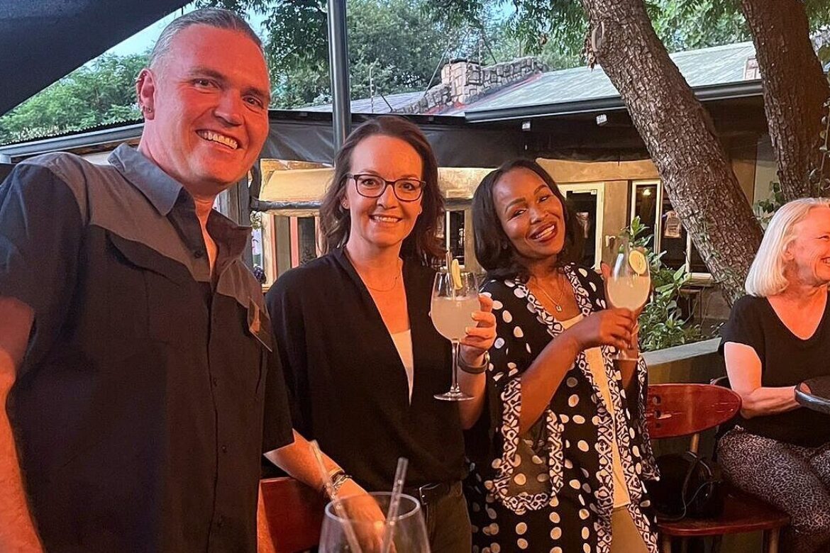 A group of four singles from the Singles Cooking Club stands outside at a table, smiling and holding drinks. With trees and a building in the background, they enjoy a relaxed, social atmosphere perfect for single events.