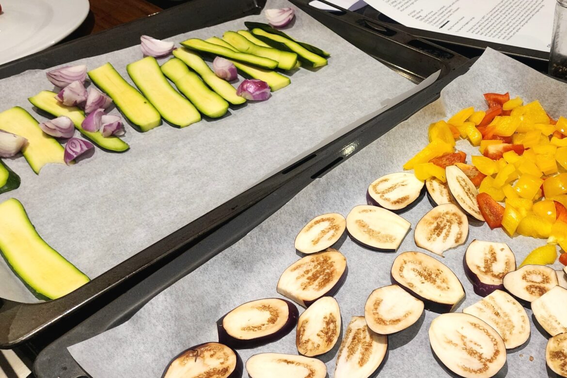 At the Singles Cooking Club, sliced zucchini, shallots, eggplant, and vibrant bell peppers lie on parchment-lined trays, ready for roasting.