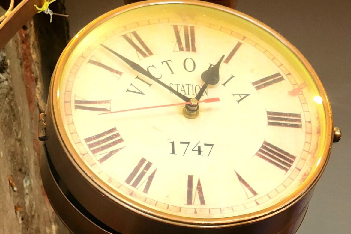 A vintage-style wall clock with Roman numerals and the text Victoria Station, 1747 complements the exposed brick of a rustic indoor setting. The hands point to 10:10, perfect for starting a singles food tour with its timeless charm.